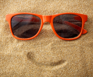 orange sunglasses on sand with smile outline drawn with finger